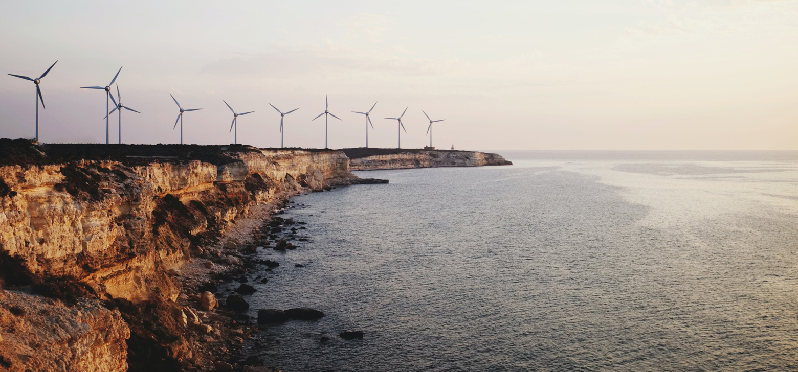 Windmills line the edge of a seaside cliff at dusk. 